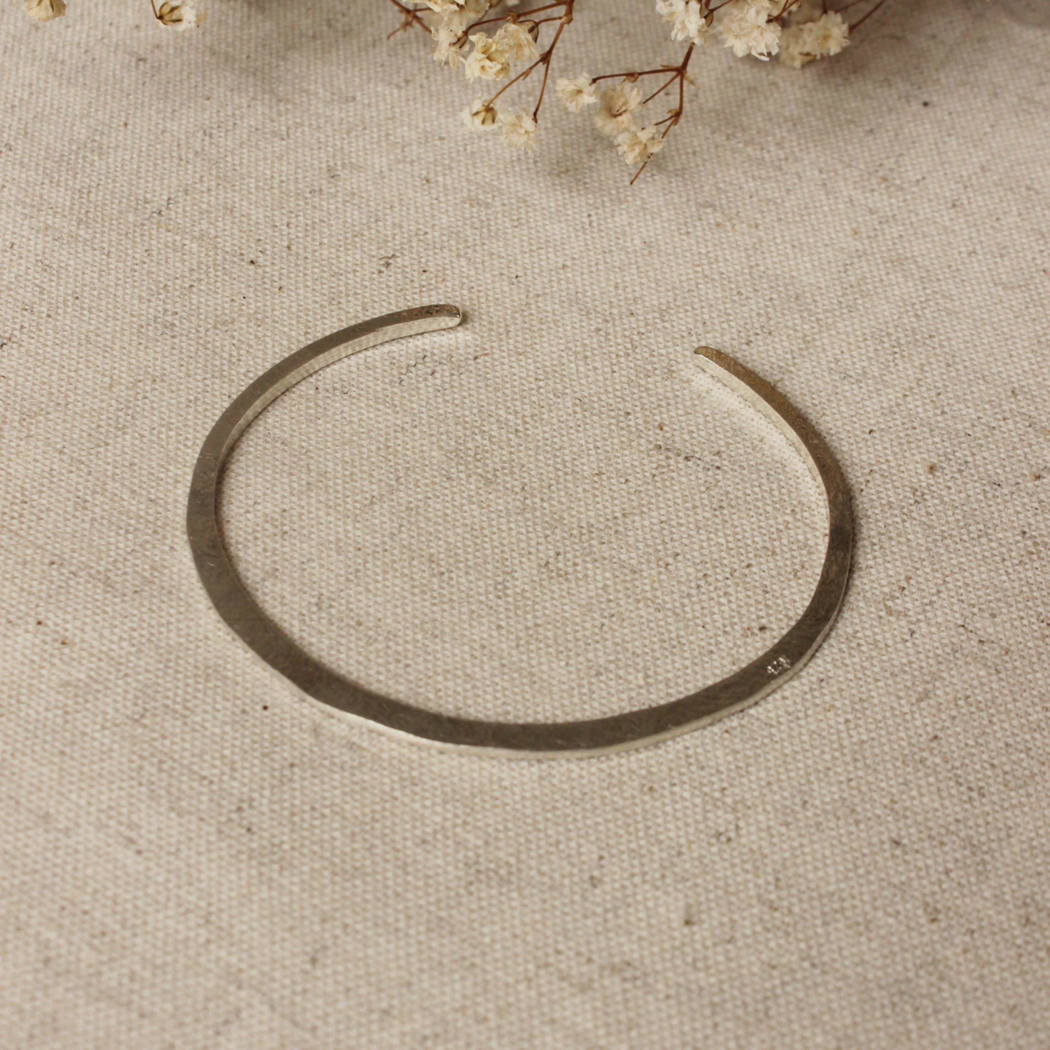 This delicate silver bangle is hammered flat and features a soft texture on one side and a smooth texture on the other side. This bangle is fully adjustable and ready to fit all wrist sizes.