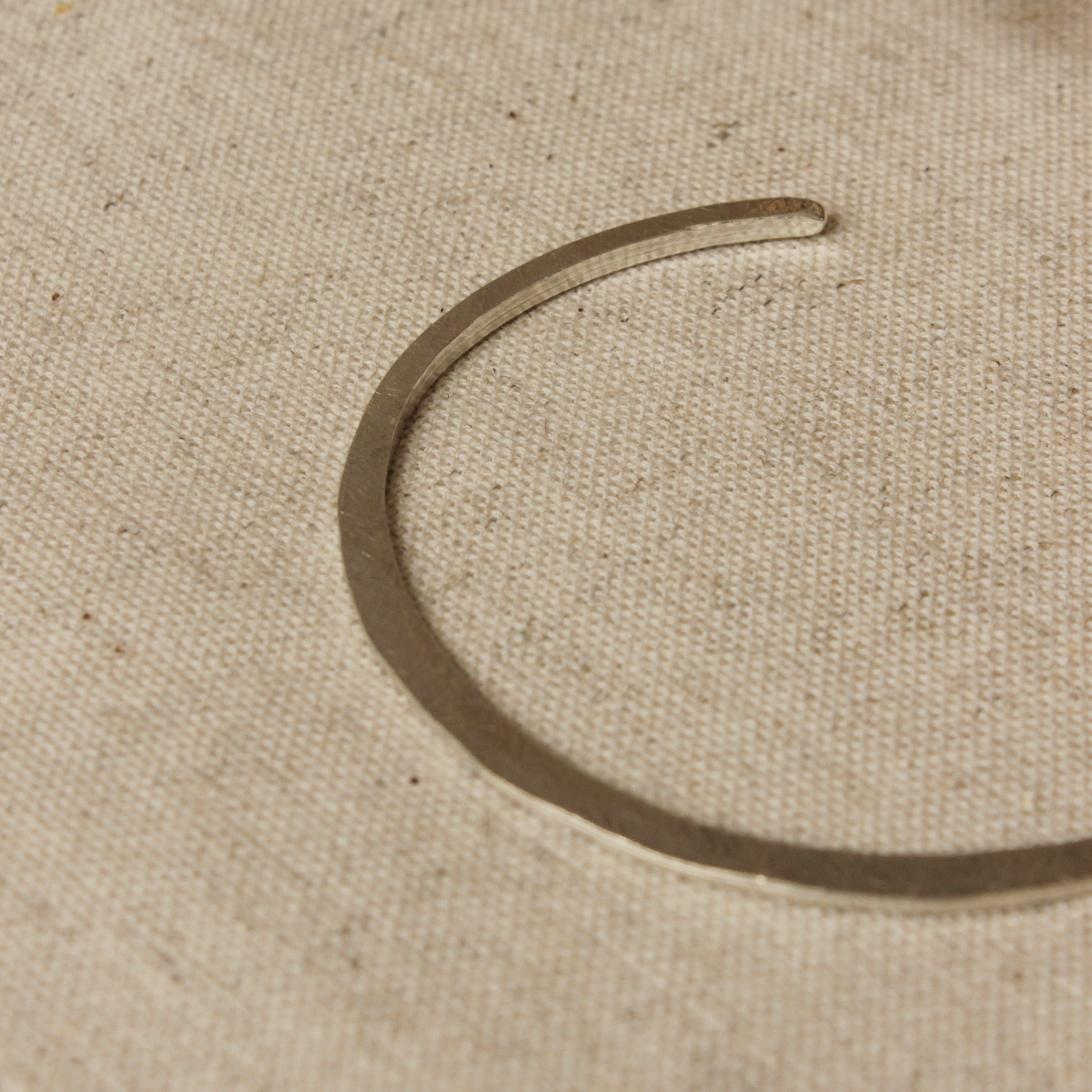 This delicate silver bangle is hammered flat and features a soft texture on one side and a smooth texture on the other side. This bangle is fully adjustable and ready to fit all wrist sizes.
