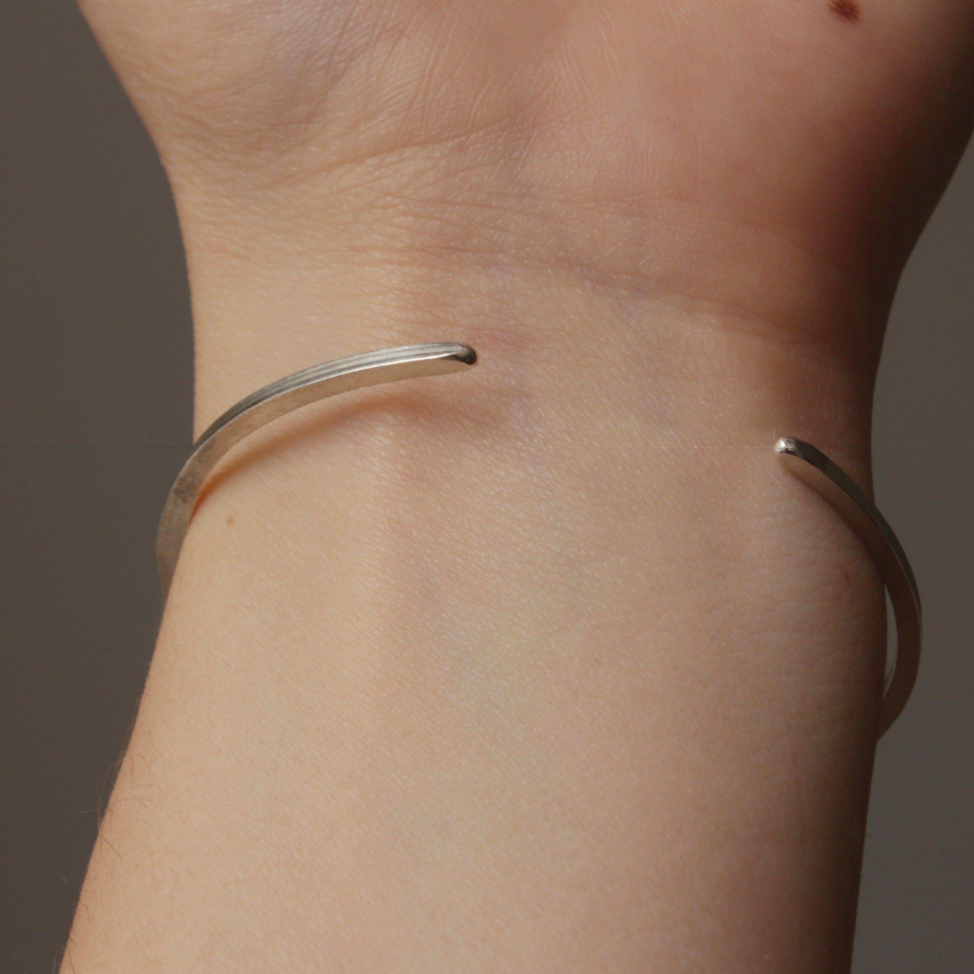 This delicate silver bangle is hammered flat and features a soft texture on one side and a smooth texture on the other side. This bangle is fully adjustable and ready to fit all wrist sizes.