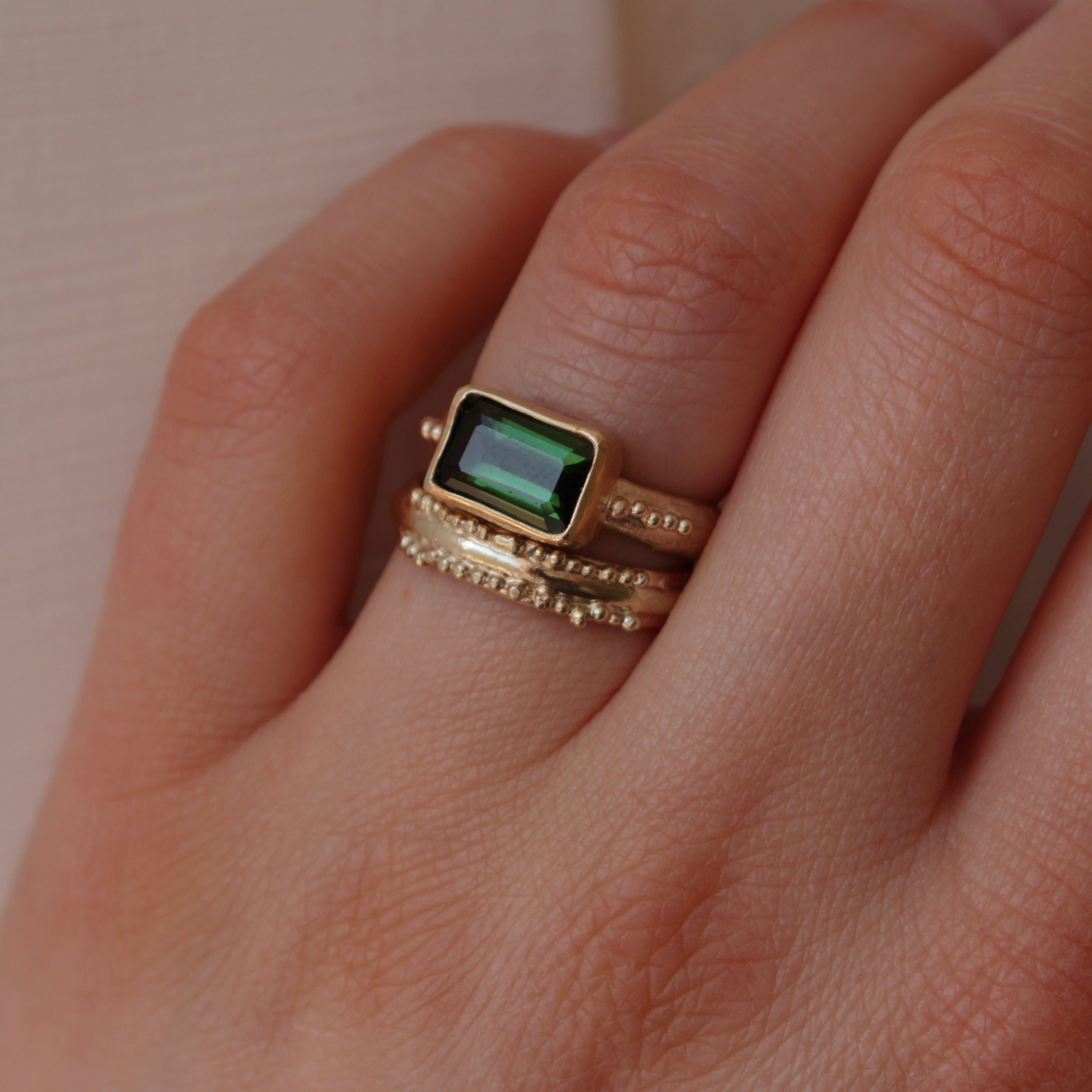 A stunning Green Tourmaline stone set on a 9 ct gold band. The band features an organic textures with tinny gold granules delicately framing the centrepiece stone.. Hand crafted alternative engagement ring by Josie Mitchell jewellery. Made in Frome, Somerset. Worn with the Ancient wedding band in 9 ct gold.