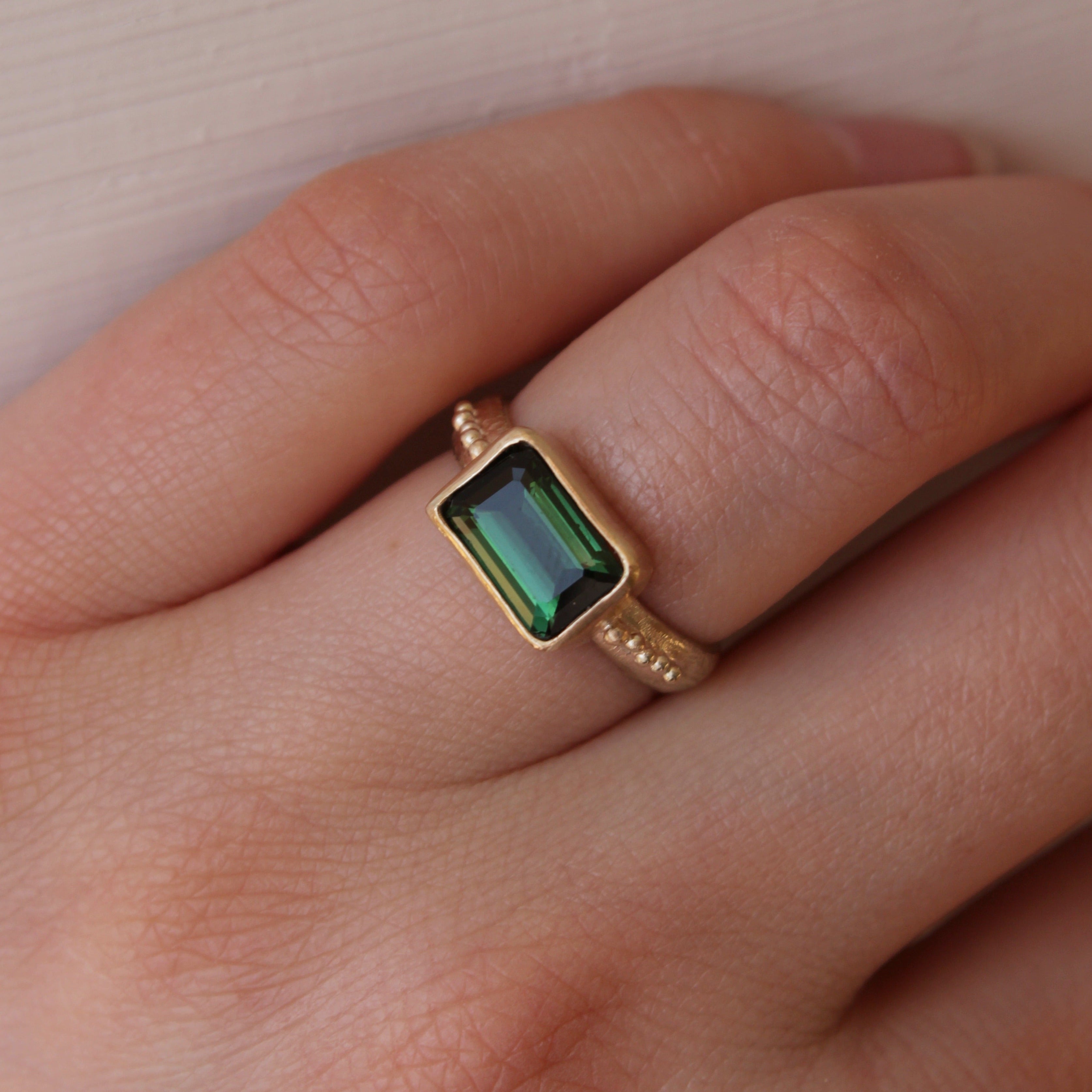 A stunning Green Tourmaline stone set on a 9 ct gold band. The band features an organic textures with tinny gold granules delicately framing the centrepiece stone.. Hand crafted alternative engagement ring by Josie Mitchell jewellery. Made in Frome, Somerset.