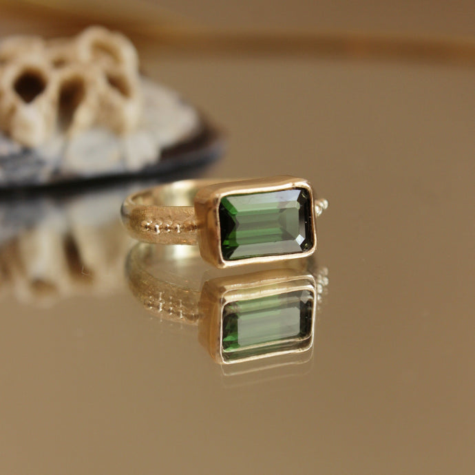 A stunning Green Tourmaline stone set on a 9 ct gold band. The band features an organic textures with tinny gold granules delicately framing the centrepiece stone.. Hand crafted alternative engagement ring by Josie Mitchell jewellery. Made in Frome, Somerset. 