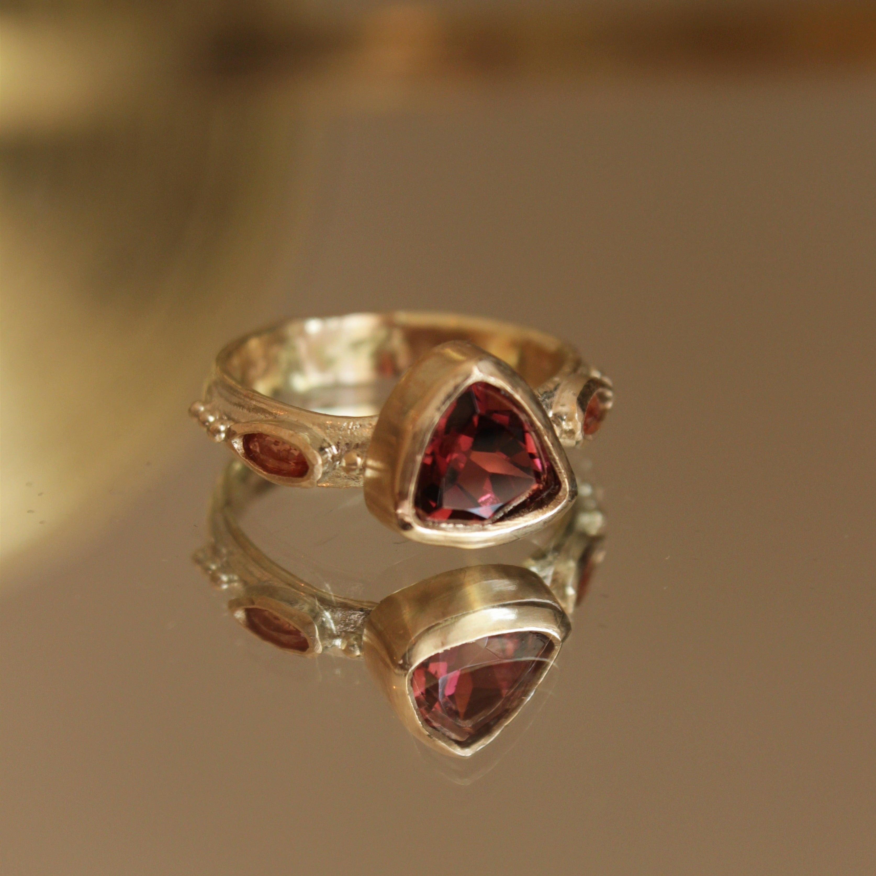 Alternative pink tourmaline engagement ring, handcrafted by Josie Mitchell jewellery in Frome, Somerset. Featuring a stunning deep pink tourmaline stone with peach coloured sapphires on either side and delicate gold granules.