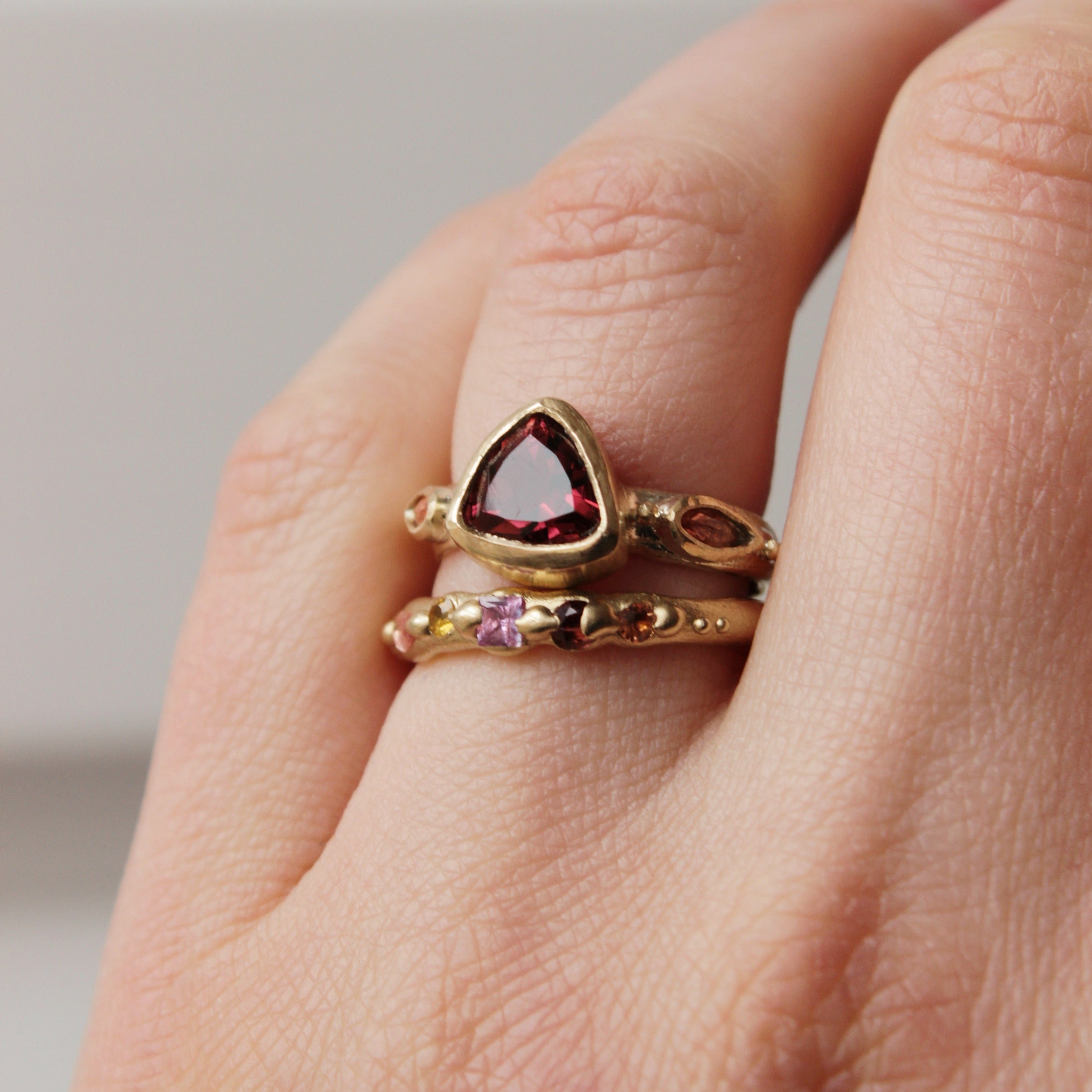 Alternative pink tourmaline engagement ring, handcrafted by Josie Mitchell jewellery in Frome, Somerset. Featuring a stunning deep pink tourmaline stone with peach coloured sapphires on either side and delicate gold granules. Worn with the Sapphire wedding band